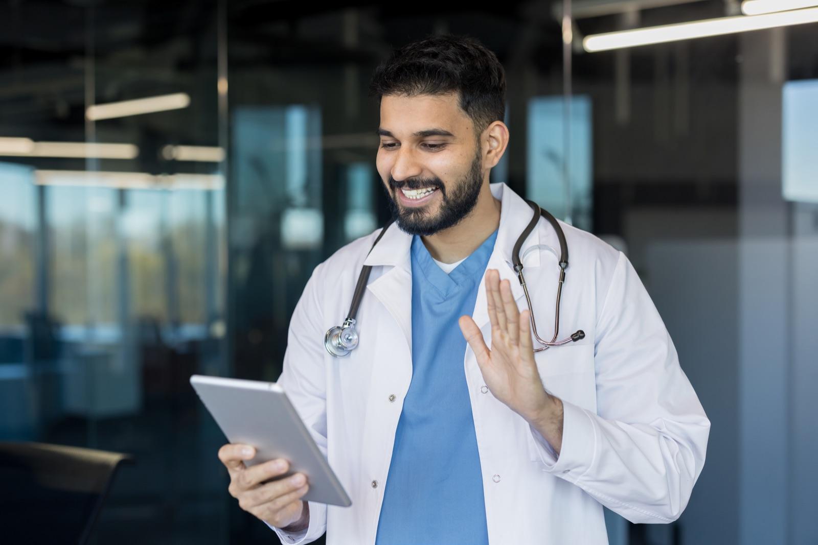 A doctor greets a patient on a video call from a tablet